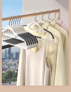 Close-up of white non-slip hangers with grey pads holding silk dresses on a golden rod