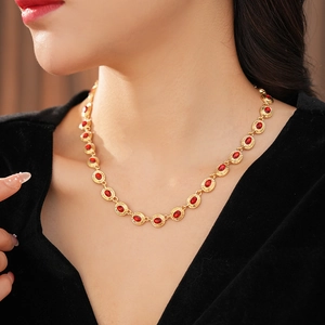Gros plan d'un collier vintage doré avec maillons ovales et pierres rouges sur cou