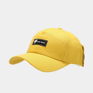 Detailed close-up of a bright yellow cotton baseball cap featuring a 'HAND MADE' woven patch
