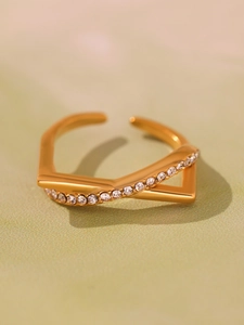 Detailed close-up of golden crisscross ring with white zircons on olive background