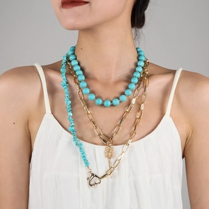 Close-up of layered turquoise bead necklace with a gold relief pendant and thick links