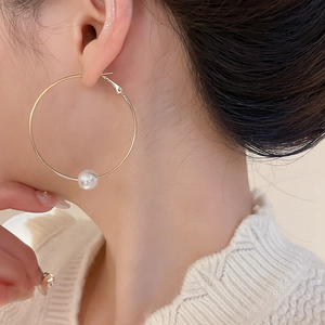 Close-up of a large gold hoop earring with a white pearl on a model in a white sweater