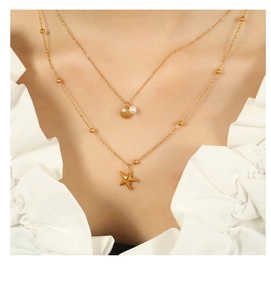 Detailed shot of double-layered gold necklace featuring a starfish and shell pearl pendant