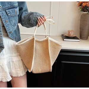 Beige woven straw tote bag with long handles styled in a casual summer lifestyle setting