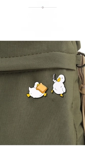 Detail of funny white duck enamel pins with knife and toast on green canvas bag