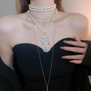 Macro detail of multilayer pearl necklace with diamond-encrusted cross pendant