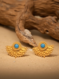 Detail of fan-shaped gold earrings with blue turquoise stones on a natural sand background