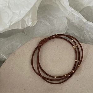 Detailed close-up of dark brown multi-layered elastic hair tie with golden bead accents