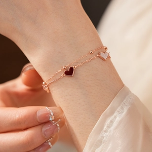 Gros plan d'un bracelet double couche en or rose avec des pendentifs en forme de cœur en émail