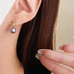 Detail of vintage 18k gold plated stud earrings with black pearl and zircon bow on model
