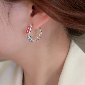 Detail of silver C-shaped hoop earring with pink and blue enamel B letter patterns