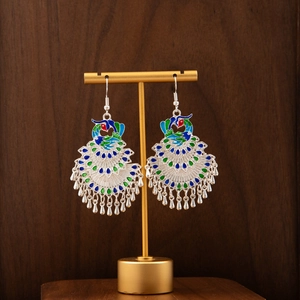 Detail of peacock enamel earrings with silver-finish bells on a golden display stand