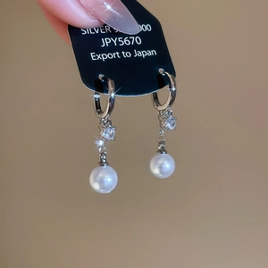 Detailed view of silver hoop earrings with zircon and dangling white pearls