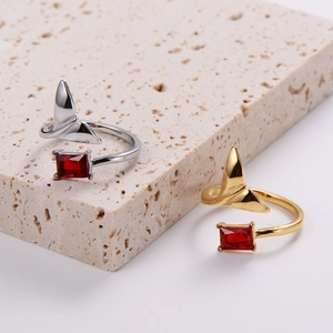 Detail of silver and gold fish tail rings with red zircon on porous stone pedestal