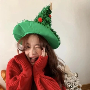 Sparkly green Christmas tree hat with red ornaments worn by a model in a cozy festive setting