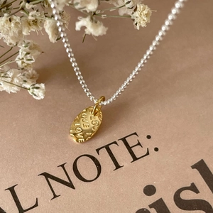 Close-up of gold LOVE pendant on mixed silver and gold chain with dry flower background