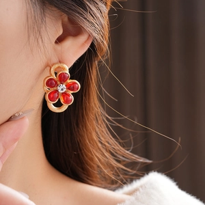 Close-up of model wearing gold flower earrings with red glass petals and center diamond