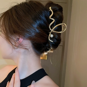 Detail view of a gold metallic wavy hair claw with a white pearl on a model's hair