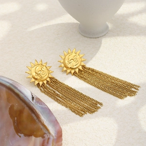 Detail of 18K gold-plated sun and moon earrings with long chain tassels on a stone background