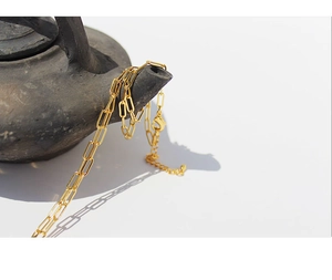 Detail of gold-plated paperclip chain necklace draped on a vintage ceramic pot