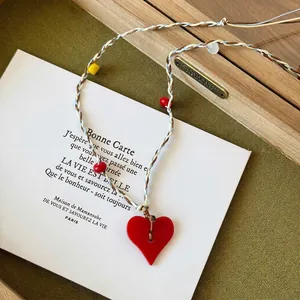 Detail of red heart pendant necklace with multi-color braided cord and colorful beads