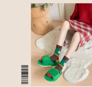 Detail of green plush slippers with festive Christmas socks worn on a white fur rug