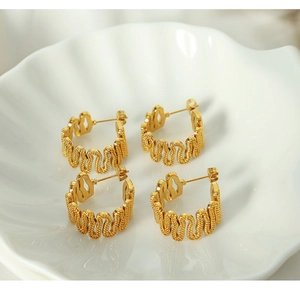 Detailed view of gold C-shape wavy earrings displayed on a white shell plate