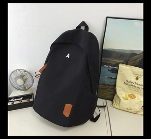 Detail of black canvas backpack featuring white A print and leather tag on a desk
