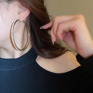Close-up of a silver-colored oversized hoop earring with pavé rhinestones on a model