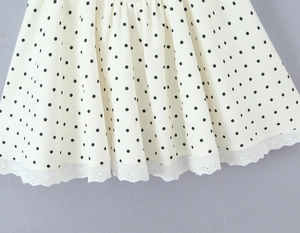 Detail of polka dot dress featuring cream fabric and intricate black lace hem stitching