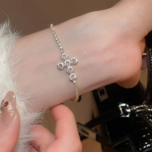 Close-up of a gold cross bracelet with pink and white cubic zirconia on a wrist