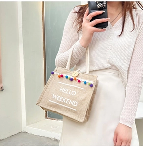Detail of linen handbag with HELLO WEEKEND text, colorful pom-poms and wooden button