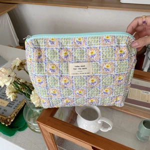 Detailed close-up of quilted floral makeup bag with blue zipper and textile label
