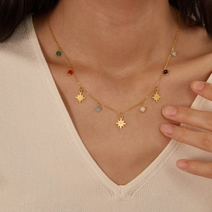 Detail of gold titanium necklace with star charms and colorful beads on a model