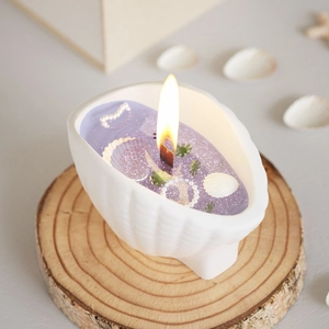 Close-up of a conch shell candle with purple glitter wax and burning wood wick
