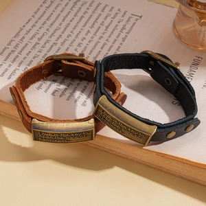 Vintage leather bracelet with engraved bronze metal plaque on a retro book background