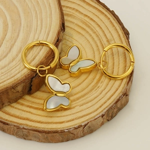 Boucles d'oreilles papillon dorées avec incrustation en nacre sur fond de bois naturel