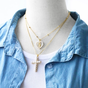 Close-up of layered gold necklaces with pearl heart and cross pendants on a mannequin