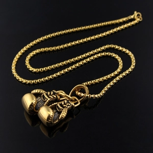 Macro detail of gold boxing glove pendant necklaces with vintage finish on black background