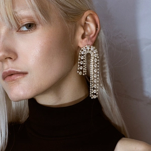 Elegant gold U-shaped tiered rhinestone earrings worn by a model on black background