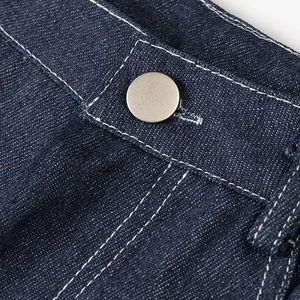 Détail du tissu denim bleu foncé avec bouton en métal argenté et surpiqûres blanches