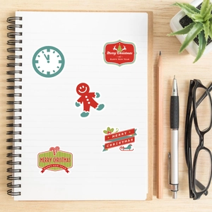 Five assorted Christmas stickers with Merry Christmas and Happy New Year on an open notebook