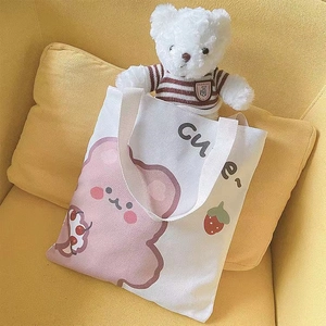 Cute bear and strawberry print on off-white canvas tote bag against yellow sofa
