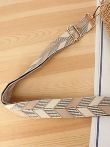 Adjustable geometric woven bag strap with golden metal hooks on a wooden table