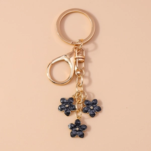 Close-up of golden keychain with three black flower charms on a soft beige background