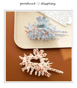 Detail showing two large coral-shaped hair claws in blue and cream with artistic ink patterns