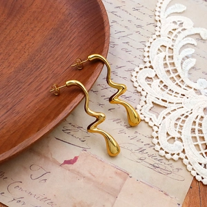 Détail macro de boucles d'oreilles dorées irrégulières sur un plateau en bois vintage