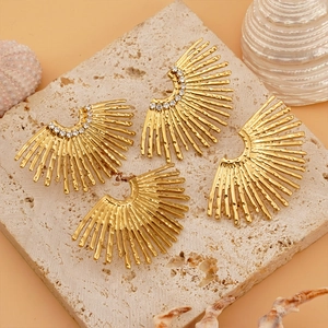 Golden sunburst fan stud earrings with cubic zirconia on a natural stone background