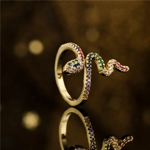 Golden snake-shaped open ring featuring colorful zircon stones on a dark reflective surface