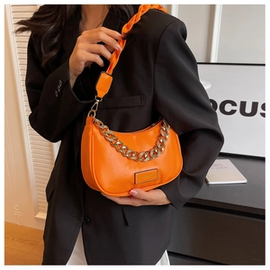 Detail of bright orange crescent bag with bold gold chain and woven shoulder strap